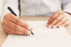 A person writing on paper with a pen.