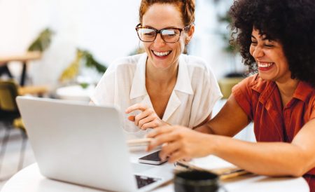 Two women sitting at a table looking at a laptop.